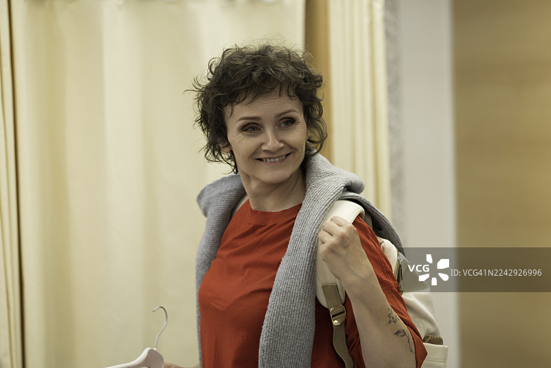 身着红色上衣、围巾和包包的微笑女子在商店里，展现休闲时尚与购物好心情图片素材