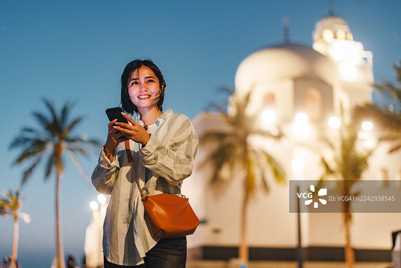 一位快乐的女性正用智能手机探索标志性的清真寺图片素材