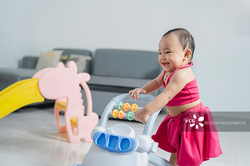 开心的女婴在室内推着玩具助行器图片素材