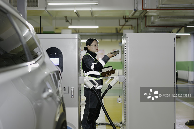 一位亚裔女性电气工程师正在检查电动汽车充电站。图片素材
