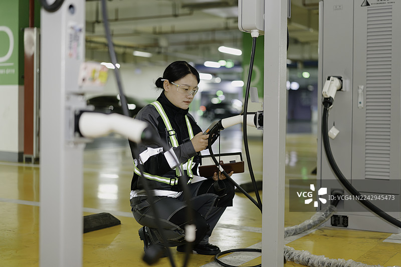 一位亚裔女性电气工程师正在检查电动汽车充电站。图片素材