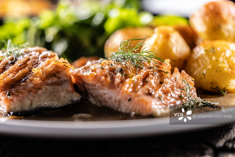 浅盘中盛放着两片烤三文鱼，淋有蘑菇酱和莳萝，旁边搭配烤土豆和新鲜生菜沙拉。图片素材