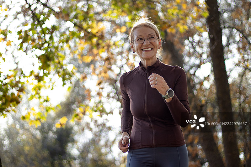 一位成熟的金发女子在美丽的阳光明媚的秋日里，在自然环境中慢跑。图片素材