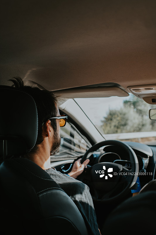 一名戴着橙色墨镜的男子在晴朗的一天驾驶一辆左舵车。图片素材
