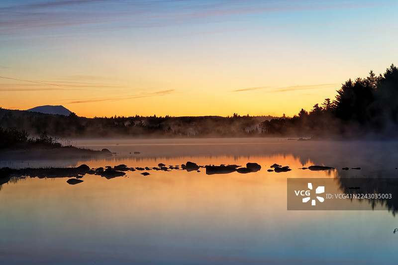 日落时分，薄雾笼罩着宁静的湖泊风景，远处是森林剪影，位于美国格林维尔图片素材