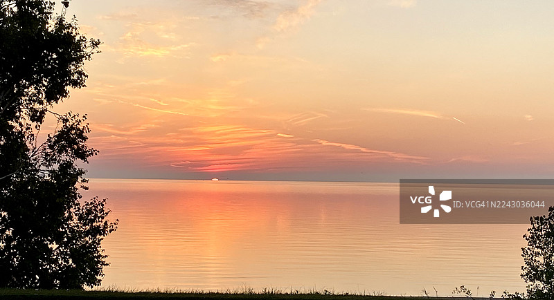 夕阳下的宁静湖景，橙色天空与剪影树木图片素材
