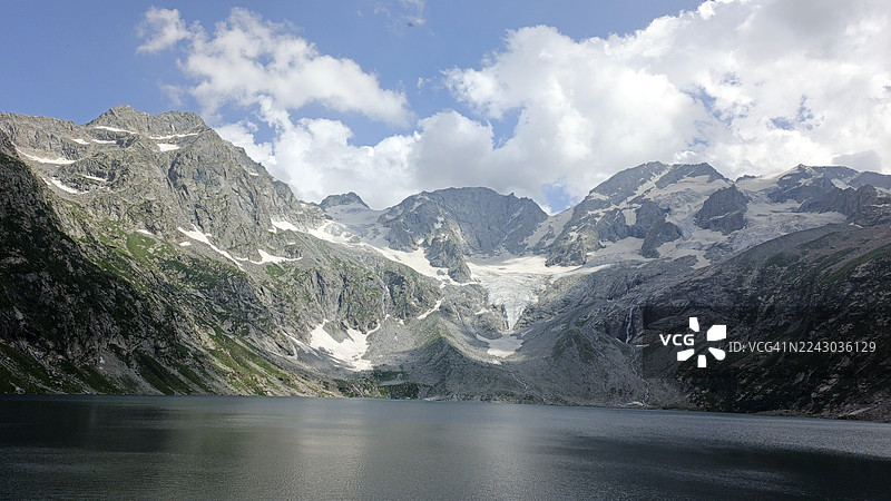 白雪皑皑的山脉倒映在宁静的湖水中，天空多云，巴基斯坦，库姆拉特山谷图片素材