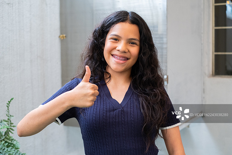 一位年轻的拉丁裔少女微笑着看着镜头，竖起大拇指。图片素材