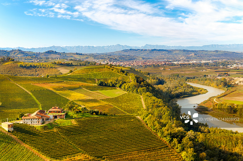 从高处俯瞰农田和葡萄园，一条蜿蜒的河流和远处的山峦在蓝天下，意大利，巴巴雷斯科图片素材