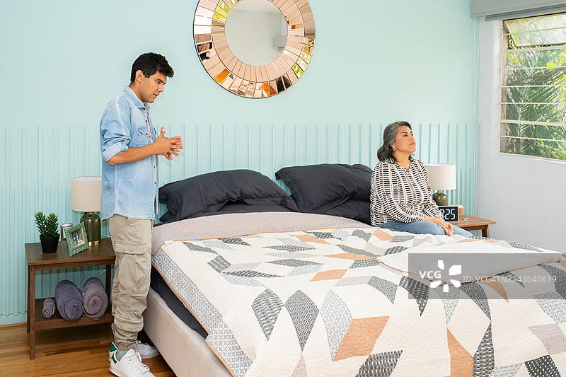 一对拉丁裔夫妇在墨西哥城家中卧室里争吵，女子坐在床上，男子站着图片素材