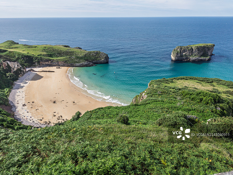 西班牙，绿色悬崖间一处美丽沙滩的高角度视图，拥有绿松石般的海水和远处的独立岩柱，天空晴朗。图片素材