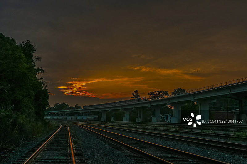 空荡荡的铁轨在戏剧性的日落天空下蜿蜒伸向远方，高架公路结构与其平行延伸，佐治亚州多拉维尔图片素材