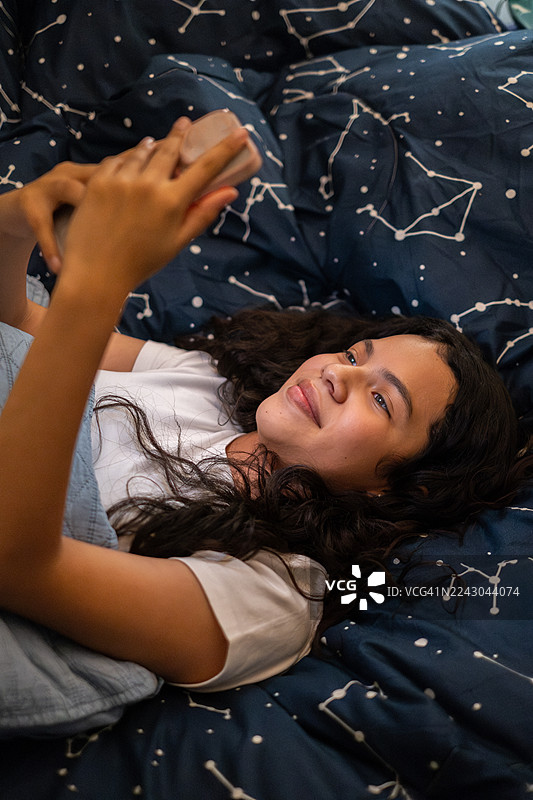 年轻的拉丁裔女孩晚上躺在床上玩手机——墨西哥，墨西哥城图片素材