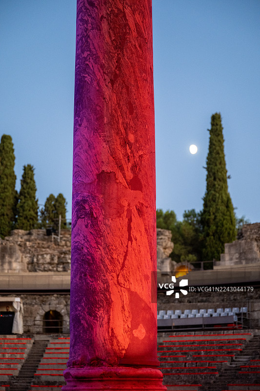 古罗马柱在有满月的暮色天空下，被鲜艳的红紫色灯光照亮，俯瞰着一个圆形剧场图片素材