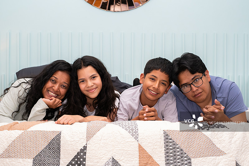 拉丁情侣与他们年幼的青春期儿子和女儿躺在床上，面带微笑地看着镜头 - 墨西哥城，墨西哥图片素材