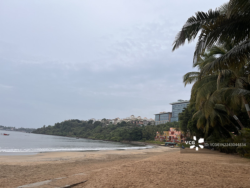 阴天下的宁静热带海滩，有棕榈树和远处的度假村图片素材