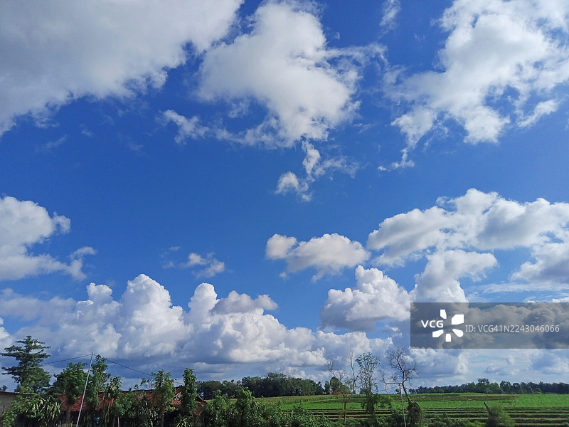 晴朗天气下，郁郁葱葱的绿色乡村风光之上，是拥有蓬松白云的广阔蓝天图片素材