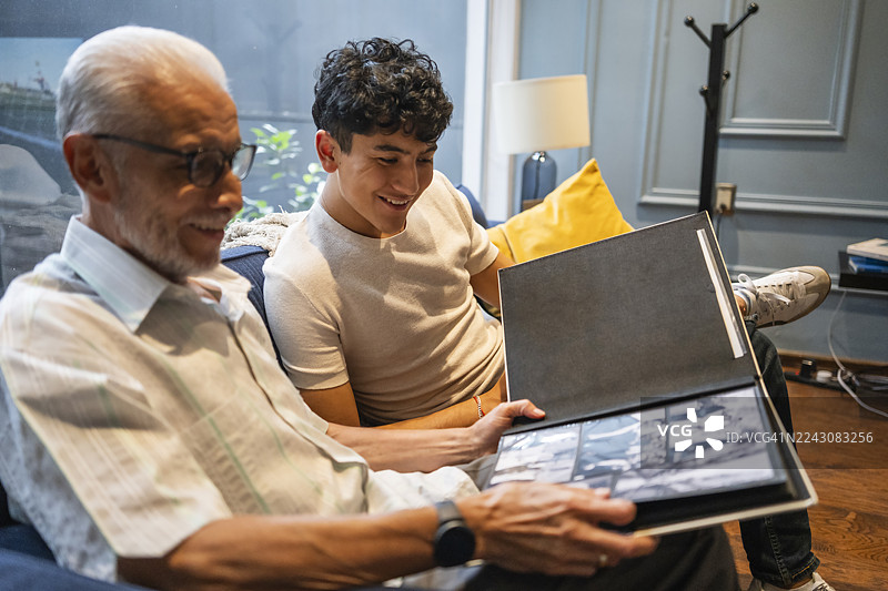 爷爷向孙子展示相册，重温并分享过去的珍贵回忆。图片素材