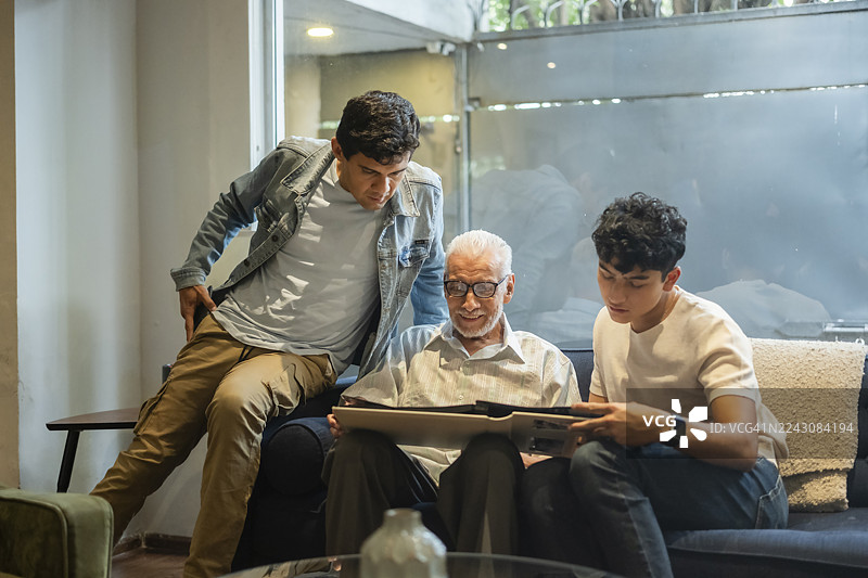 一位老人向儿子和孙子展示相册，分享其中蕴含的记忆，追忆着他生命中逝去的时光。图片素材
