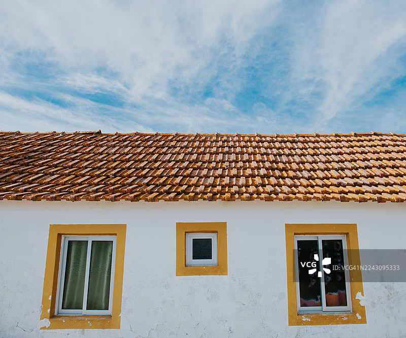 低角度拍摄的葡萄牙传统住宅，带有陶瓦屋顶和黄色装饰的窗框。图片素材