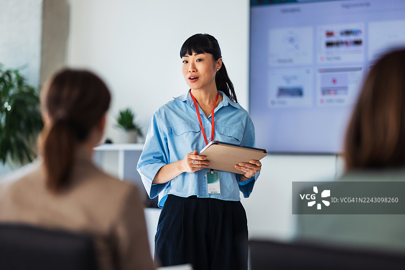 专业演讲者手持平板电脑在明亮的办公室进行团队简报会议图片素材