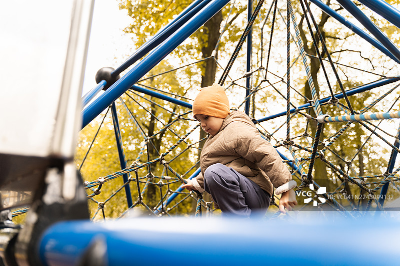 秋季游乐场里，一个孩子在绳索结构上玩耍攀爬，玩得不亦乐乎图片素材