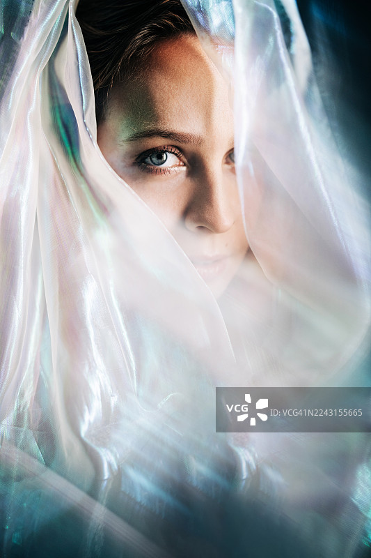 一位女士直视镜头，她面部被一层发光、珠光宝气、半透明的织物部分遮挡并勾勒。图片素材