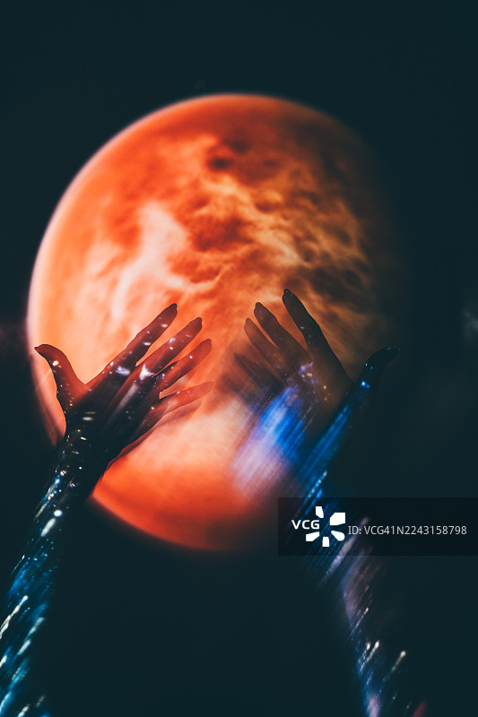 特写镜头，两只手投射着充满活力的蓝色星系图案，背景是模糊的红色行星。图片素材