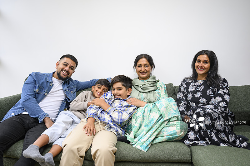 三代英裔巴基斯坦家庭在沙发上，面向镜头微笑图片素材