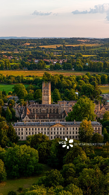 日落时牛津大学玛德琳学院的鸟瞰图,拥有标志性的中世纪塔楼和古典立面,周围环绕着树木和乡村景观,体现了旅行和建筑设计的遗产与学术概念。图片素材