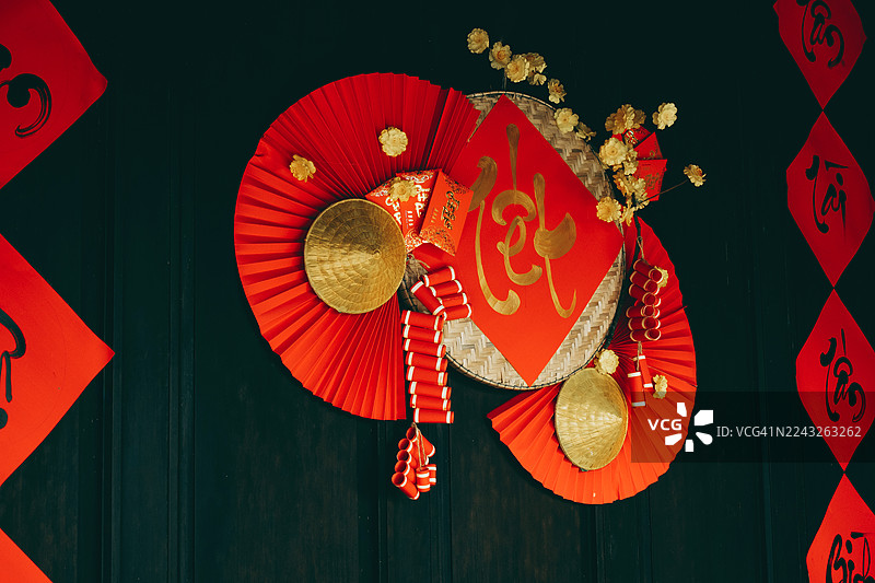 深色木墙上的传统亚洲新年装饰，包括红扇、鲜花、金帽子和书法。图片素材