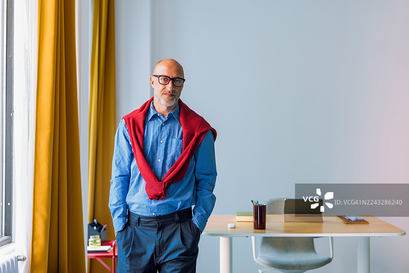 穿着红色毛衣的专业男士，毛衣搭在肩上，在现代办公室的办公桌前图片素材