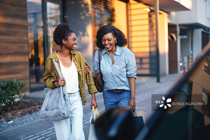 一群朋友在城市街道上购物，脸上带着笑容，提着购物袋，享受着一天的外出时光。图片素材
