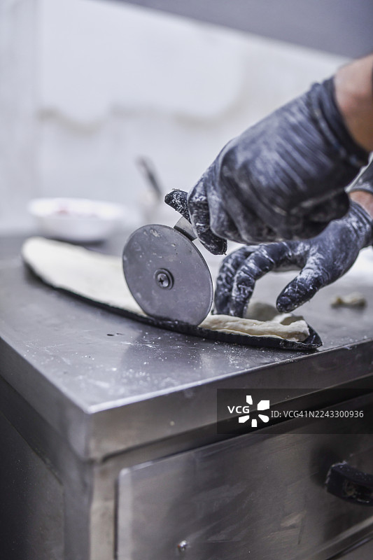 专业厨师在不锈钢厨房工作室用披萨刀擀面团图片素材