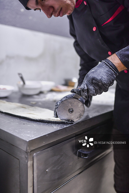 专业厨师在不锈钢厨房工作室用披萨刀擀面团图片素材