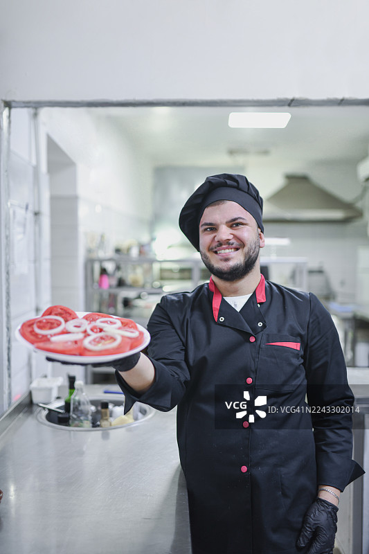 大厨在明亮的厨房里展示新鲜番茄沙拉，提供友善的服务和温馨的用餐氛围图片素材
