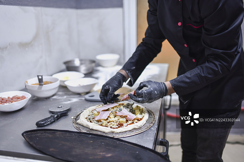 厨师在厨房里准备披萨，添加食材，制作新鲜的手工餐点图片素材