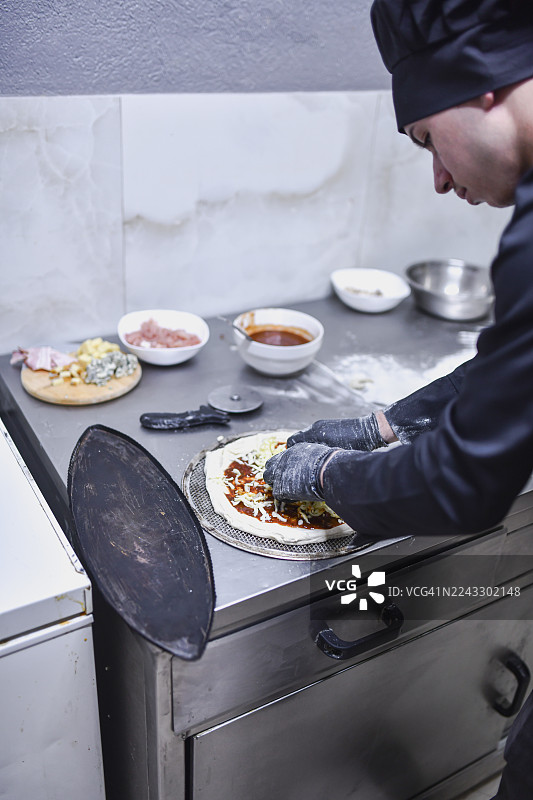 厨师在专业厨房的不锈钢台面上准备新鲜披萨，上面放着配料图片素材