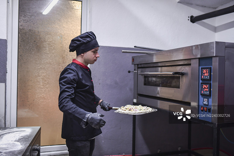 厨师在专业的厨房环境中操作工业烤箱烘烤披萨图片素材