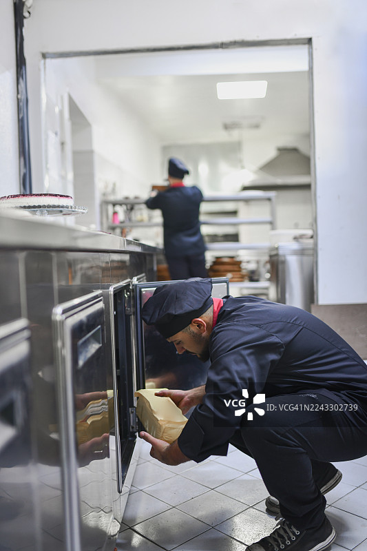 厨师在繁忙的商业厨房里，跪在厨房储物区，手中拿着纸袋图片素材