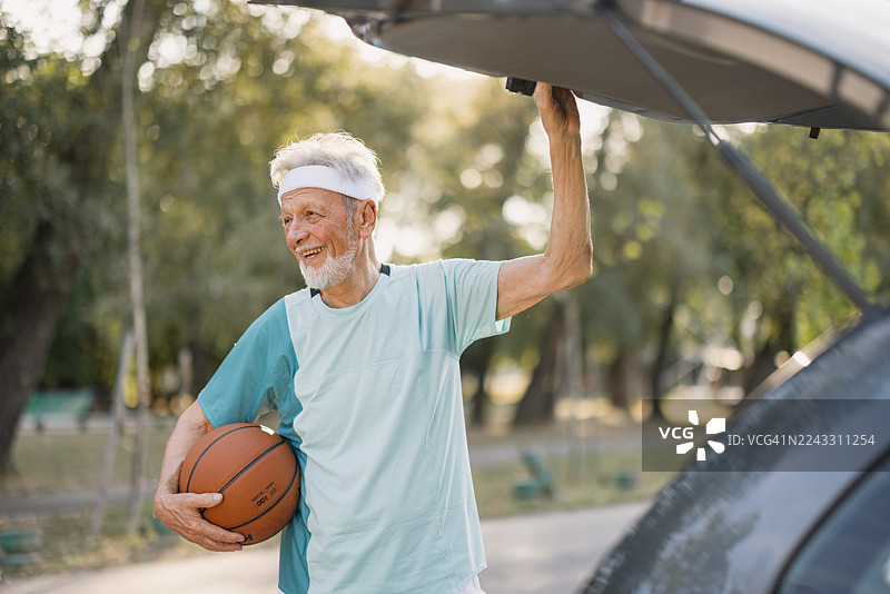 一位年长的男士面带微笑，手里拿着篮球，站在汽车后备箱旁图片素材
