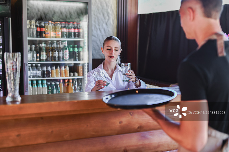 现代俱乐部里，女调酒师正在为服务员准备酒杯的吧台场景图片素材