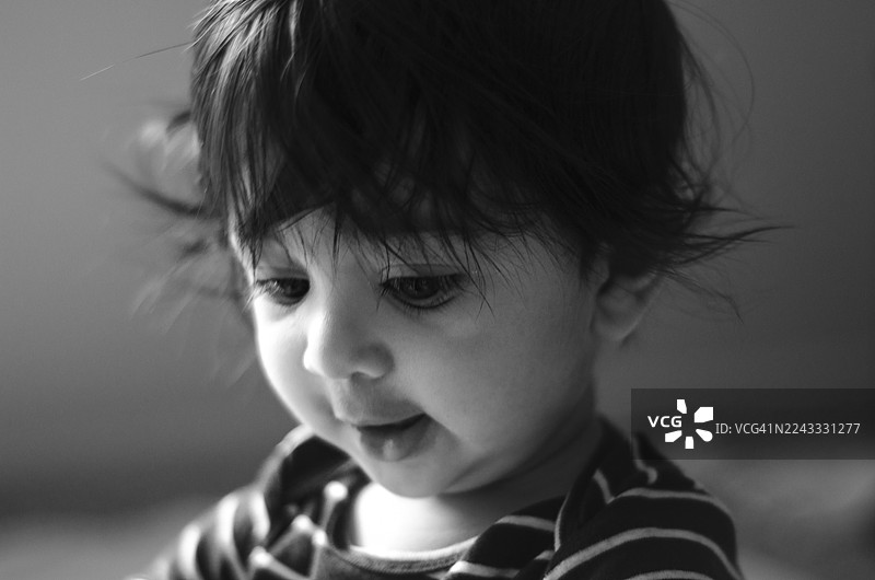 静谧的发现：一个可爱的印度小男孩，带着温柔的好奇心，在黑白照片中向下看。特写肖像。图片素材