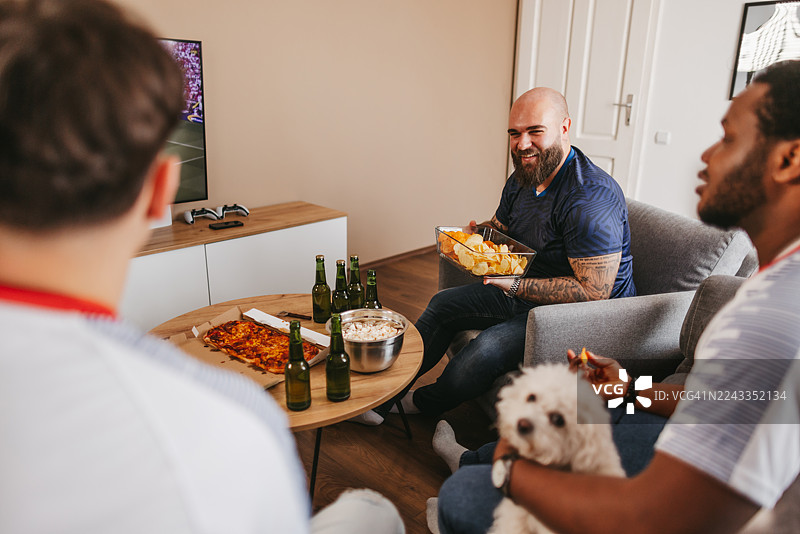 三个年轻男子在家看电视上的体育比赛图片素材