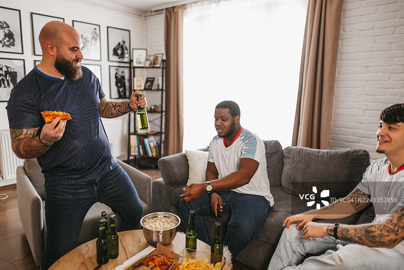 快乐的男性朋友们在家中边看电视比赛边享用啤酒和小吃图片素材