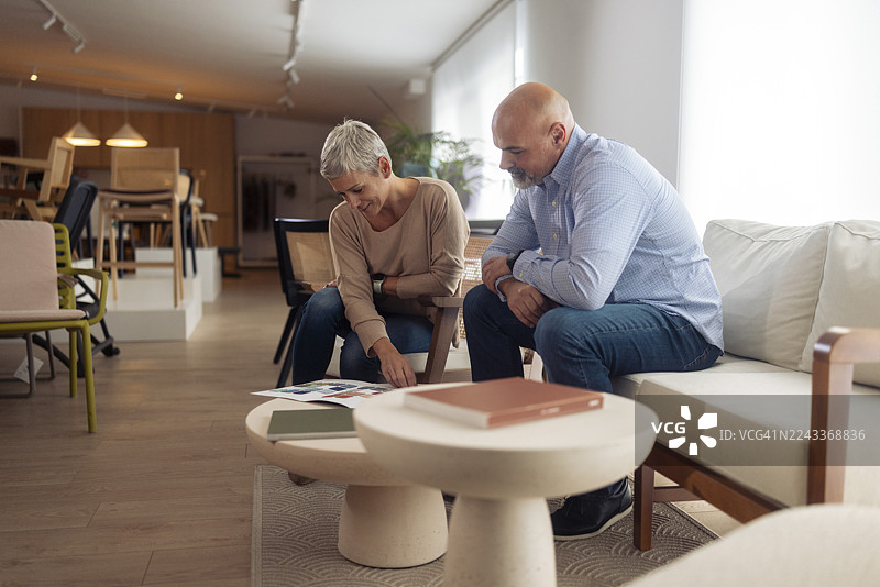 一对X世代夫妇穿着休闲服装，坐在现代椅子上，一起翻阅彩色目录图片素材