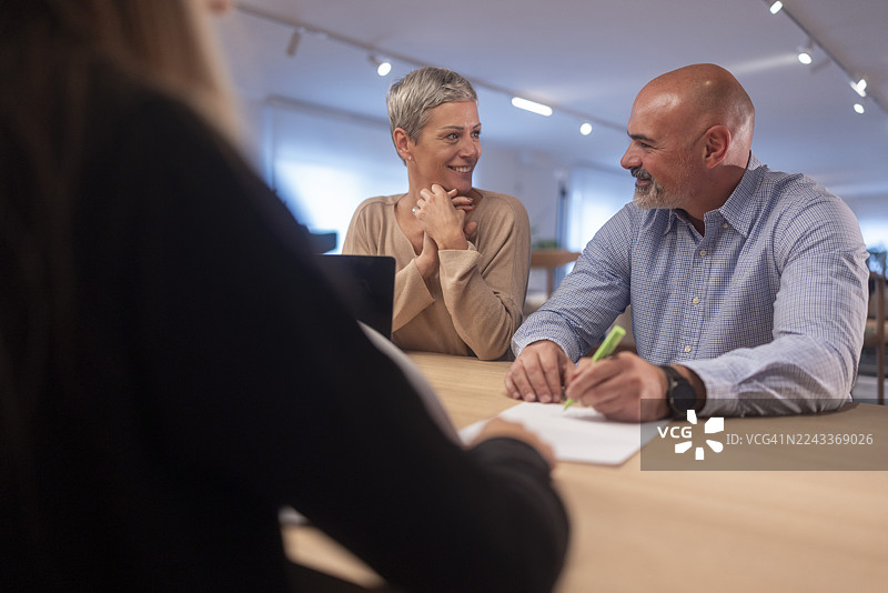 一位白发女子和她秃头的丈夫正在展厅的桌子旁最终确定家具购买事宜，丈夫正在签署文件。图片素材
