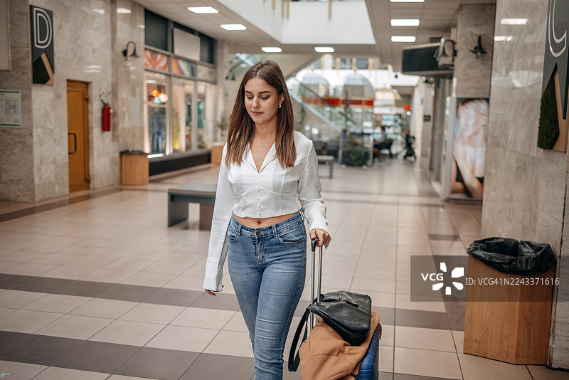 一位女士拖着行李箱走在酒店休息室，看起来很开心图片素材