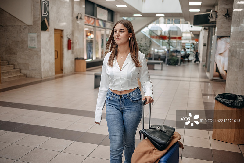 一位女士拖着行李箱走在酒店休息室，看起来很积极乐观。图片素材