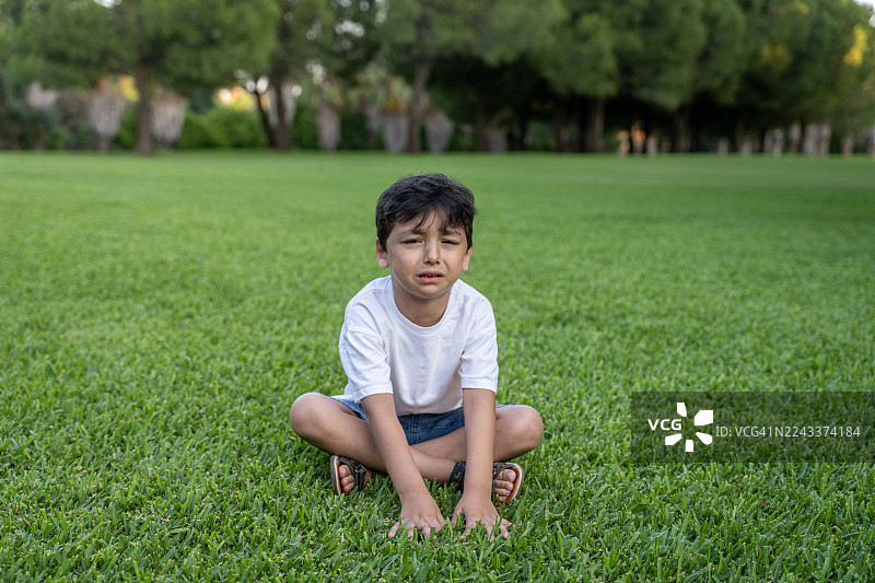 伤心的小男孩坐在公园的草地上图片素材